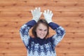 Young cute beautiful girl in a sweater on the background of a boardwalk holds hands at the head depicts antlers of a deer