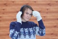 Young cute beautiful girl in a sweater on the background of a boardwalk listens to music with headphones on his head holds his Royalty Free Stock Photo