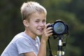 Young cute blond child boy taking picture with tripod camera on