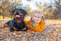 Young cute blonde girl child and her German Rottweiler dog lying and posing in autumn leaves. Friendship, pet and kid. Royalty Free Stock Photo