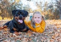 Young cute blonde girl child and her German Rottweiler dog lying and posing in autumn leaves. Friendship, pet and kid. Royalty Free Stock Photo