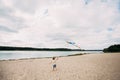 A young cute boy with a kite in his hands runs along the sandy beach on the banks of a picturesque river Royalty Free Stock Photo