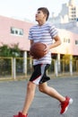 A young cute boy plays basketball at the outdoor streetball court on a sunny summer day. Teenager player in action dribbling