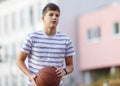 Young cute boy plays basketball at the outdoor streetball court on a sunny summer day. Teenager player in action dribbling