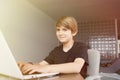 Young cute boy using laptop computer while sitting at the table in living room at home. Look at camera. Royalty Free Stock Photo