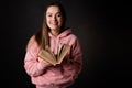 A young cute brunette in a pink hoodie, reading a book. Student with an open book in her hands, Royalty Free Stock Photo