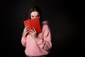 A young cute brunette in a pink hoodie, reading a book. A student with an open book in her hands, Royalty Free Stock Photo