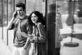 Young cute couple - a boy and a girl standing near a glass building. The couple spend time together. The guy speaks on the phone, Royalty Free Stock Photo