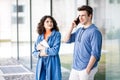 Young cute couple - a boy and a girl standing near a glass building. The couple spend time together. The guy speaks on the phone, Royalty Free Stock Photo