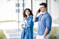 Young cute couple - a boy and a girl standing near a glass building. The couple spend time together. The guy speaks on the phone, Royalty Free Stock Photo