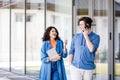 Young cute couple - a boy and a girl standing near a glass building. The couple spend time together. The guy speaks on the phone, Royalty Free Stock Photo