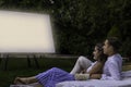 Young cute couple embracing sitting in the garden in a date night watching a movie in the outdoor cinema in summer Royalty Free Stock Photo