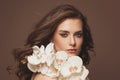 Young cute female face with healthy brown hair, clear skin, natural makeup and white orchid flowers portrait Royalty Free Stock Photo