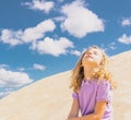 Young cute girl in hat sitting on the sand beach. Fashion model girl posing on the sand dunes. Blue summer sky as Royalty Free Stock Photo