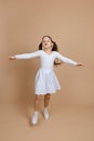 Young cute girl with long dark hair in white dress, socks and gymnastics shoes whirling, dancing, spreading hands