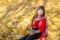 Young cute girl sitting in the Park among the autumn leaves with a cup of hot tea, Royalty Free Stock Photo