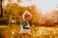 Young cute girl in sun glasses walking on a glade with dandelions. Sunset.