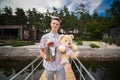 A young cute guy is waiting for a meeting with his girlfriend. Waiting on the pier with champagne and a teddy bear. Romantic date