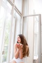 Young and cute lady sitting on the windowsill and looking out th Royalty Free Stock Photo