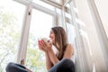 Young and cute lady sitting on the windowsill and looking out th