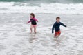 Young cute little boy and girl playing at the seaside running into the surf on a sandy beach in summer sunshine Royalty Free Stock Photo