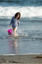 Young cute little girl playing at the seaside carrying a red bucket at the edge of the surf on a sandy beach in summer Royalty Free Stock Photo