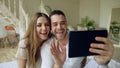 Young cute and loving couple having video chat holding tablet computer and chatting to parents sitting in bed at home Royalty Free Stock Photo