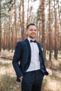 Young cute man in a white shirt business suit with a bow tie is standing on the nature in the park and smiling Royalty Free Stock Photo