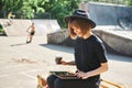 Young cute modern millennial hipster girl in hat dressed in black relax and work in Skatepark.