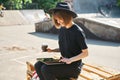 Young cute modern millennial hipster girl in hat dressed in black relax and work in Skatepark.