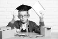 Young cute pupil boy in grey sweater and glasses sitting at desk with copybook in hand wooden numbers pink piggy pig Royalty Free Stock Photo