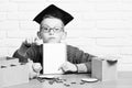 Young cute pupil boy in grey sweater and glasses sitting at desk with copybook in hand wooden numbers pink piggy pig Royalty Free Stock Photo