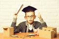 Young cute pupil boy in grey sweater and glasses sitting at desk with copybook in hand wooden numbers pink piggy pig Royalty Free Stock Photo