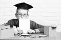 Young cute pupil boy in grey sweater and glasses sitting at desk with copybook in hand wooden numbers pink piggy pig Royalty Free Stock Photo