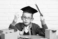 Young cute pupil boy in grey sweater and glasses sitting at desk with copybook in hand wooden numbers pink piggy pig Royalty Free Stock Photo