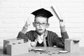 Young cute pupil boy in grey sweater and glasses sitting at desk with copybook in hand wooden numbers pink piggy pig Royalty Free Stock Photo