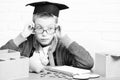 Young cute pupil boy in grey sweater and glasses sitting at desk with copybook wooden numbers pink piggy pig bank in Royalty Free Stock Photo