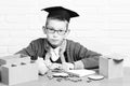 Young cute pupil boy in grey sweater and glasses sitting at desk with copybook wooden numbers pink piggy pig bank in Royalty Free Stock Photo