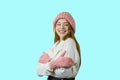 Young cute red-haired teen girl in a knitted pink hat and mittens is standing in a half-turn, hugging herself with cute Royalty Free Stock Photo