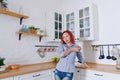 Young cute redhead curly woman 30 in blue jeans and a shirt sitting and relaxing in her bright clean kitchen. Healthy happy lifes Royalty Free Stock Photo