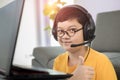 Young and cute 10s little Asian boy wearing headphone sitting in living room and using laptop notebook computer for online Royalty Free Stock Photo