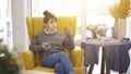 A young girl sitting in a big chair with a phone listening to music drinking tea