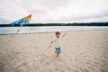 smiling boy with a kite in his hands runs along the sandy beach on the banks of a picturesque river Royalty Free Stock Photo