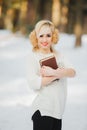 Young cute stylish modern girl holding book in fabulous magic fantasy winter cold snowy forest. Nature lover. Happy cheerful