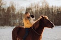 Young happy cute smiling woman with her dog border collie sit on horse in snow field on sunset. yrllow dress Royalty Free Stock Photo
