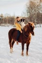 Young happy cute smiling woman with her dog border collie sit on horse in snow field on sunset. yrllow dress