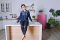 Young cute woman 30+ with short hair in blue jeans and a shirt sitting and relaxing in her clean kitchen Royalty Free Stock Photo