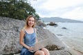 Young cute woman using laptop and sitting on stone near sea, empty morning beach. Royalty Free Stock Photo