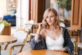 Young cute woman using phone sits in cafe at table with smartphone, answering Royalty Free Stock Photo