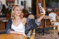 Young cute woman using phone sits in cafe at table with smartphone, answering Royalty Free Stock Photo